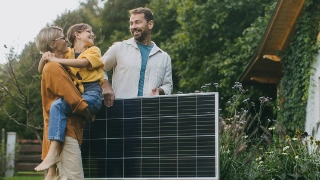 Familie vor Ihrem Eigenheim mit einem Solarpanel.